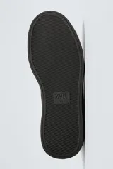 Zapatilla de estilo urbano confeccionada en piel con acabado de serraje. Presenta un diseño minimalista con cordonera oculta y suela de goma a contraste.