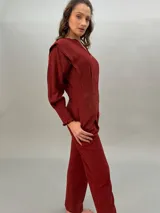 Mono largo color ladrillo de crepe de lana liviana, con corte entallado en la cintura, bolsillos laterales y mangas largas con detalle de volados en los puños. Presenta una moldería superior que enmarca los hombros como si fuera un chaleco.