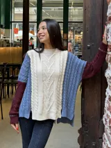 Sweater de punto con diseño color block que combina paneles en color crema, azul y bordó. Presenta un tejido con textura de ochos, cuello redondo, mangas largas y un corte holgado con el ruedo trasero más largo que el delantero.