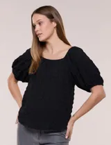 Blusa blanca de tela texturada y silueta fluida, con escote en U y frunces. Cuenta con mangas cortas abullonadas con elástico en los puños y ruedo redondeado.