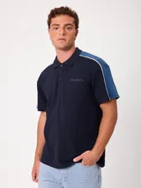Remera polo Rusty de manga corta, color azul marino con paneles en tono azul acero en los hombros, ribetes blancos y logo bordado en el pecho.
