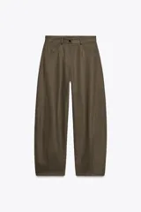 Pantalón de tiro medio color verde oliva, confeccionado en tejido con estructura de espiga. Presenta pierna ancha, trabillas en la cintura, cinco bolsillos y cierre frontal con cremallera y botón.