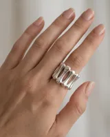 Anillo ancho de acero plateado con diseño de barras paralelas y pequeñas aplicaciones brillantes.