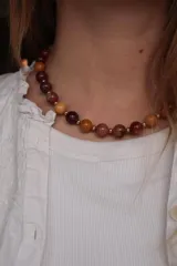 Collar corto de piedras naturales de moakaita en tonos borgoña, mostaza y marrón, separadas por pequeñas cuentas doradas.