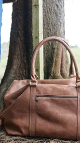 Bolso de viaje marrón de cuero napa fulonada, con doble asa de mano y cierre superior con cremallera.