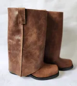 Bota de cuero marrón con diseño 2 en 1, que incluye una polaina desmontable. Presenta una caña alta estructurada y una base de bota tipo botineta con suela plana de goma negra.