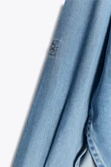 Camisa de denim de corte oversize con cuello solapa, manga larga con puños, cierre frontal con botones a presión y bolsillos de plastrón en el delantero.