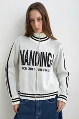 Campera tejida de algodón en color bordó y blanco, con cuello alto, cierre frontal completo y diseño con estampado tipográfico.