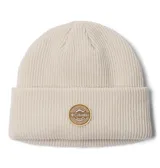 Gorro tipo beanie de tejido de punto acanalado en color beige claro, con diseño de puño doblado y parche circular con el logo de Columbia en el centro.