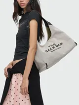 Bolso tipo hobo Marc Jacobs The Belted Sack de lona color beige, con inscripción frontal en negro "THE SACK BAG MARC JACOBS". Cuenta con asa de hombro y correa ajustable de cuero negro.