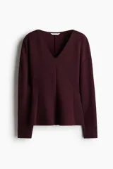 Top bordó de tejido efecto neopreno, con escote en V, hombros caídos y mangas largas. Cuenta con un diseño entallado en la cintura que se ensancha levemente hacia el ruedo.