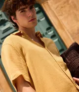 Camisa de manga corta color mostaza, confeccionada en algodón con textura, cuello inglés y cierre frontal de botones.
