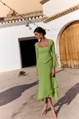 Vestido midi verde claro con efecto dos piezas, compuesto por un corset con escote cuadrado y costuras frontales estructuradas, y falda midi fluida de corte asimétrico. Cuenta con mangas largas semitransparentes.
