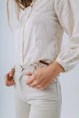 Camisa de algodón bordada color blanco con diseño floral sutil, cuello redondo, mangas abullonadas y cierre frontal de botones de nácar.