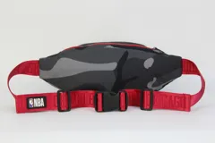 Riñonera con estampado de camuflaje en tonos grises, con logo del equipo de baloncesto Chicago Bulls en el frente. Tiene correa roja ajustable con hebilla de plástico y cierre de cremallera roja.