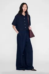 Camisa vaquera de manga corta y corte ligeramente boxy, confeccionada en denim de algodón color azul marino con textura lisa y tejido diagonal. Cuenta con cuello clásico, cierre frontal con botones metálicos y doble pespunte.