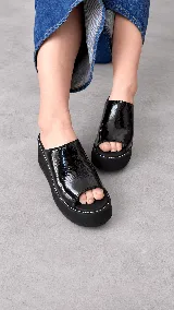 Zuecos Dakota de plataforma corrida, color negro en charol, con capellada amplia y costuras pespunteadas en blanco alrededor de la suela.