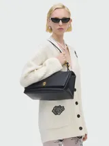 Cartera de hombro Marc Jacobs, modelo The Large Dual, en color negro. Presenta una estructura rígida con solapa frontal, cierre de giro metálico dorado y asa superior fija.