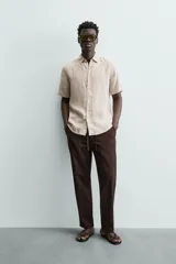 Camisa de lino color beige de corte relajado, con cuello solapa, manga corta y cierre frontal con botones.