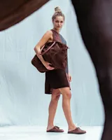 Bolso de mano tipo duffel de gran capacidad, confeccionado en gamuza color chocolate. Presenta doble asa corta superior y correa larga ajustable para llevar al hombro o cruzada.