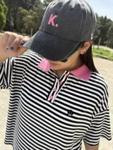 Gorro de gabardina color gris con visera curva y bordado de la letra K en color rosa.