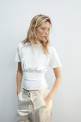Camiseta blanca de algodón con cuello redondo, manga corta y diseño ajustado en la cintura tipo corset.