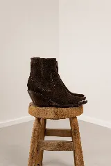 Bota corta de estilo western confeccionada en cuero vacuno color marrón oscuro, con taco cuadrado de madera y puntera metálica decorativa.