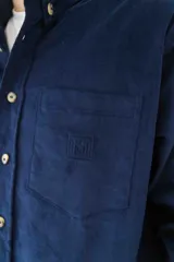 Camisa de pana azul marino de manga larga con cuello abotonado, cierre frontal con botones color hueso, bolsillo de parche en el pecho izquierdo y logo bordado en el bolsillo.