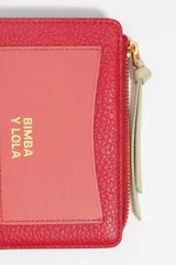 Billetera compacta de cuero vacuno en color negro, con cierre superior metálico dorado y logo de la marca estampado en el frente.