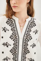 Camisa blanca de manga larga con cuello mao y cierre frontal de botones. Presenta delicados bordados florales en tonos neutros a lo largo de la parte frontal y en los hombros.