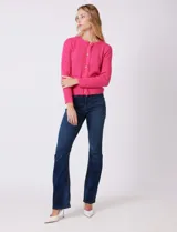 Cardigan de punto color fucsia, con escote a la base, cierre frontal con botones metálicos dorados y terminaciones desflecadas. Presenta bolsillos simulados en la parte delantera y mangas largas.