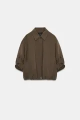 Chaqueta bomber color marrón, con cuello solapa, cierre frontal oculto con cremallera y botones a presión. Presenta mangas remangadas con trabillas y bajo abullonado con elástico interior.