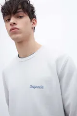 Buzo gris de felpa liviana con cuello redondo, mangas largas y puños ajustados. Tiene un bordado pequeño en el pecho y un diseño estampado en la espalda.