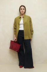 Camisa de corte clásico y holgado, confeccionada en tela blanca, con cuello camisero, cierre frontal de botones de nácar y mangas largas con puños abotonados.