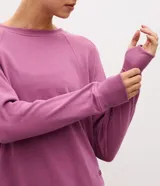 Buzo cerrado deportivo de corte oversized, color violeta, con cuello redondo, mangas largas con puños acanalados y bolsillo frontal funcional. Presenta detalles de encaje en los laterales y ruedo acanalado.