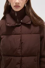 Campera híbrida con cuerpo delantero acolchado tipo puffer y mangas de tejido de punto acanalado con cuello alto. Presenta un diseño corto y holgado con cierre frontal oculto.