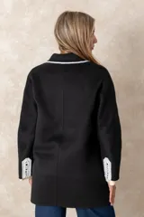 Tapado de paño negro con detalles de costuras y bordes en color blanco. Presenta un diseño de doble botonadura, solapas clásicas y corte amplio.