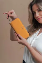 Billetera larga tipo sobre de la marca Lincoln's, confeccionada en material sintético con textura suave en color beige. Presenta un cierre perimetral metálico y el logo de la marca grabado en la parte frontal.