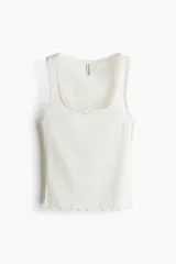 Musculosa ajustada de punto pointelle color blanco, con escote redondo, detalle de moña de satén en el centro y terminaciones con ribete de picot y ruedo con ondas.