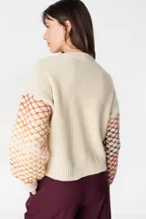 Saco de punto artesanal en color crudo, con diseño de red multicolor en mangas y laterales. Presenta cuello redondo, cierre frontal con botones y puños acanalados.