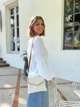 Cartera tipo sobre color crudo, confeccionada en cuero, con correa larga de cuero marrón y costuras decorativas en contraste.