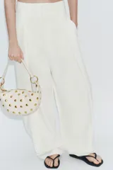 Bolso de hombro de diseño saca multiposición color blanco, decorado con tachas metálicas doradas y aros metálicos que conectan el cuerpo con la manija. Cuenta con cierre de cremallera metálica y bolsillo interior.