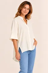Blusa de algodón color beige con diseño texturizado, cuello mao con escote en V, mangas tres cuartos y dobladillo asimétrico más largo en la parte trasera.