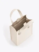 Cartera tipo tote pequeña de cuero color tostado, con doble asa superior y herrajes metálicos plateados en forma de llama en la base de las manijas. Presenta el logo de la marca estampado en la parte inferior frontal.