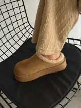 Sueco de estilo casual confeccionado en símil gamuza color marrón, con interior y borde superior revestido en corderito sintético color crema. Presenta una suela de plataforma plana de goma en tono marrón oscuro.