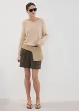 Chaleco de punto grueso color beige, de diseño recto, con cuello en V y manga larga.