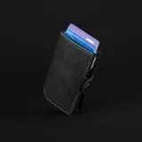 Billetera negra de cuero con caja de aluminio incorporada con sistema de deslizamiento para tarjetas, protección RFID, espacio para 5 tarjetas, sección para hasta 7 billetes y espacio adicional para libreta de propiedad y de conducir.