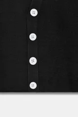 Top de punto negro de manga corta y cuello redondo, con cierre frontal de botones blancos dispuestos de forma asimétrica y ondulada.