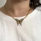 Collar dorado con dije de mariposa con alas color crema y detalles en negro.