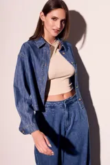 Camisa de jean azul de corte recto, con cuello clásico, cierre frontal con botones marrones, bolsillo de parche en el pecho y mangas largas con puños abotonados.